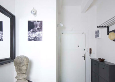 Interiér cihlového bytu, chodba, šedá dlažba, komoda, věšáky, zrcadlo, busta, fotky