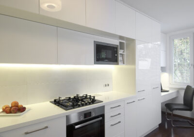 Interiér panelákového bytu, kuchyň, kuchyňská linka, bílá kuchyň, dřevěná podlaha