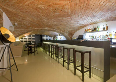 Interiér baru v Poděbradech, cihlové klenby, světlá litá podlaha, tmavé dřevo, barové židle, barový pult, osvětlené police za barem