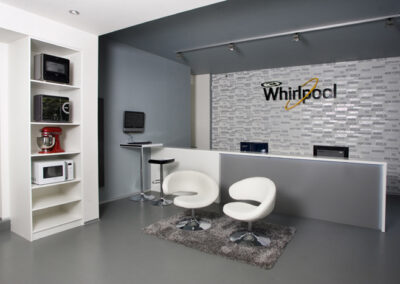 Největší showroom, zn. Whirlpool, prodejna, komerční prostor, komerční interiér, prodejní pult, spotřebiče, šedá podlaha, litá podlaha, bílá křesla, tapeta, logo na zdi