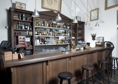 Interiér baru AnonymouS, dřevěný bar, tmavé dřevo, bar jako knihovna, barové židle, zrcadla na zdi, závěsná světla nad barem