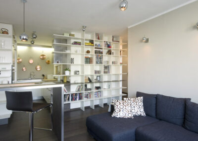 Interiér bytu Řešovská, panelákový byt, kompletní rekonstrukce, knihovna, otevřená knihovna, pohovka, barový stůl, kuchyně, kulaté osvětlení