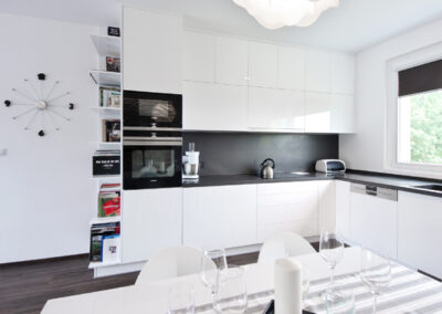 Panelákový byt, obytný prostor, obývák, vinylová podlaha, jídelní stůl, židle, světlo květina, kuchyň, kuchyňská linka, posuvné dveře, knihovna, nástěnné hodiny