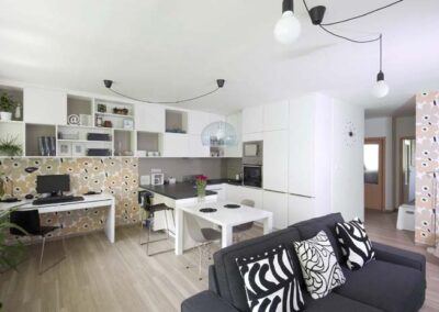 Interiér panelákového bytu, Marimekko, tapeta, kuchyň, kuchyňská linka, jídelní stůl, pohovka, skříňky nad stolem, pracovní stůl, závěsné světlo