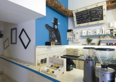 Interiér kavárny AnonymouS, grafika na zdi, dřevěný nábytek, modré pruhy, rezavý strop, nástěnné litinové umyvadlo, modrá zeď, umělecká malba, prázdné rámy