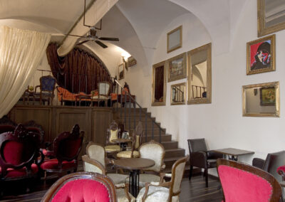 Interiér baru AnonymouS, čalouněné sezení, červená lenoška, tmavé dřevo, schodiště v pozadí, závěs v pozadí