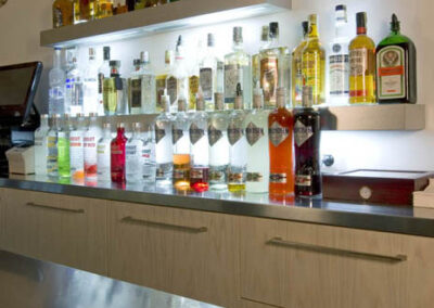 Interiér baru v Poděbradech, cihlové klenby, světlá litá podlaha, tmavé dřevo, barové židle, barový pult, osvětlené police za barem, zábaří