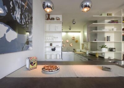 Interiér bytu Řešovská, panelákový byt, kompletní rekonstrukce, knihovna, otevřená knihovna, barový stůl, kuchyně, kulaté osvětlení, obraz na zdi, měděné pánve