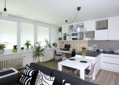 Interiér panelákového bytu, Marimekko, tapeta, kuchyň, kuchyňská linka, jídelní stůl, pohovka, skříňky nad stolem, pracovní stůl, závěsné světlo, pokojové rostliny