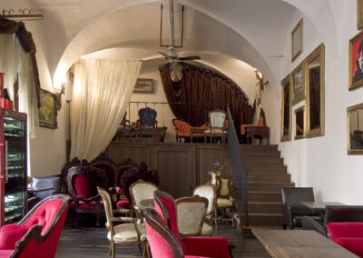 Interiér baru AnonymouS, čalouněné sezení, červená lenoška, tmavé dřevo, schodiště v pozadí, závěs v pozadí, gotické klenby, dřevěné pódium