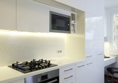 Interiér panelákového bytu, kuchyň, kuchyňská linka, bílá kuchyň, dřevěná podlaha, skříňky, pracovní kout, pracovní místo