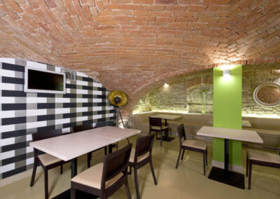 Interiér baru v Poděbradech, cihlové klenby, světlá litá podlaha, tmavé dřevo, jídelní židle, jídelní stoly, dekorativní zeď, zelený sloup