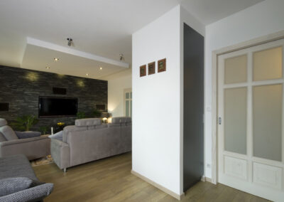 Proměna obývacího pokoje, RD Nučice, šedá pohovka, skříň v nice, černý kamenný obklad na zdi, TV na zdi