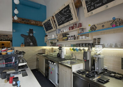 Interiér kavárny AnonymouS, grafika na zdi, dřevěný nábytek, modré pruhy, rezavý strop, nástěnné litinové umyvadlo, modrá zeď, umělecká malba