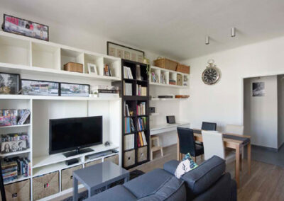 Interiér cihlového bytu, obytný prostor s kuchyní, tmavě šedá pohovka, vinylová podlaha, knihovna, pracovní kout, TV, televize, jídelní stůl