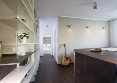 Interiér bytu Řešovská, panelákový byt, kompletní rekonstrukce, knihovna, otevřená knihovna, barový stůl, nástěnné kulaté osvětlení, kytara, béžová zeď, pohled z obývacího pokoje
