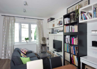 Interiér cihlového bytu, obytný prostor s kuchyní, tmavě šedá pohovka, vinylová podlaha, knihovna, pracovní kout, TV, televize, jídelní stůl