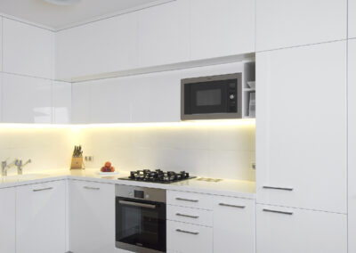 Interiér panelákového bytu, kuchyň, kuchyňská linka, bílá kuchyň, dřevěná podlaha, skříňky