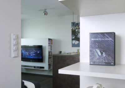 Interiér bytu Řešovská, panelákový byt, kompletní rekonstrukce, knihovna, otevřená knihovna, police, pohled z chodby do obývacího pokoje, tmavá vinylová podlaha, TV nábytek