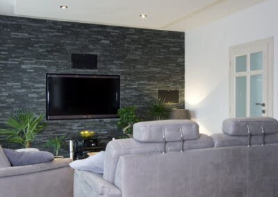Proměna obývacího pokoje, RD Nučice, šedá pohovka, černý kamenný obklad na zdi, TV na zdi, snížený podhled nad pohovkou