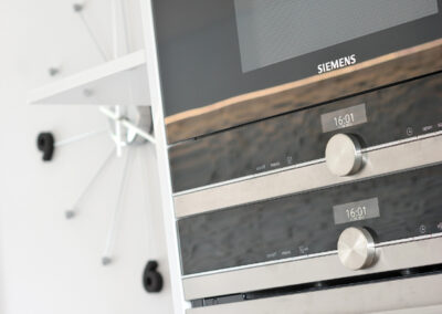 Panelákový byt, obytný prostor, obývák, kuchyň, kuchyňská linka, knihovna, nástěnné hodiny, trouba, mikrovlnka