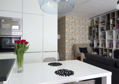 Interiér panelákového bytu, Marimekko, tapeta, kuchyň, kuchyňská linka, jídelní stůl, křeslo, knihovna, závěsné světlo, tulipány na stole