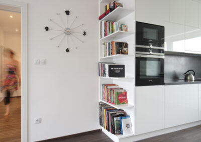 Panelákový byt, obytný prostor, obývák, vinylová podlaha, jídelní stůl, židle, světlo květina, kuchyň, kuchyňská linka, posuvné dveře, knihovna, nástěnné hodiny