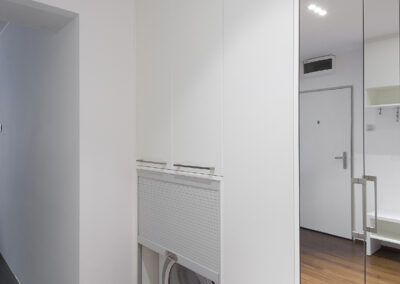 Interiér panelákového bytu, nika na sušičku, roleta, dřevěná podlaha, zrcadlová skříň, skříň se zrcadlem