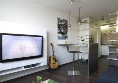 Interiér bytu Řešovská, panelákový byt, kompletní rekonstrukce, knihovna, otevřená knihovna, TV nábytek, barový stůl, kuchyně, kulaté osvětlení, obraz na zdi