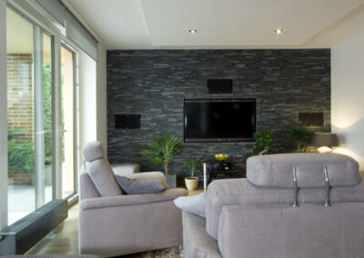 Proměna obývacího pokoje, RD Nučice, šedá pohovka, černý kamenný obklad na zdi, TV na zdi, zapuštěná TV, audio, snížený podhled nad pohovkou, vstup na terasu, francouzské okno