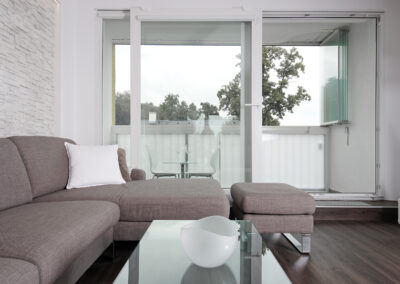 Panelákový byt, obytný prostor, obývák, vinylová podlaha, TV nábytek, konferenční stůl, velké balkonové okno, pohovka, taburet, lodžie, sezení na balkoně