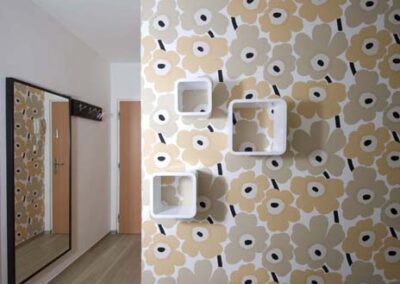 Interiér panelákového bytu, Marimekko tapeta, bílé boxy na zdi, pohled do chodby, velké zrcadlo