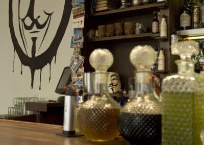 Interiér baru AnonymouS, logo na zdi, detail baru, sklenice s nápoji