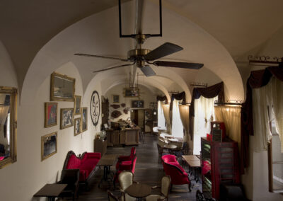 Interiér baru AnonymouS, čalouněné sezení, červená lenoška, tmavé dřevo, gotické klenby, obrazy na zdi, repliky starožitného nábytku