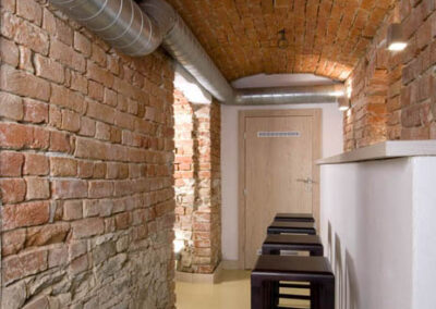 Interiér baru v Poděbradech, cihlové klenby, cihlové zdi, světlá litá podlaha, tmavé dřevo, barové židle, pult, chodba, vzduchotechnika