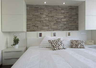 Interiér bytu Řešovská, panelákový byt, kompletní rekonstrukce, ložnice, světlá ložnice, skříně okolo postele, noční stolky, kamenný obklad za postelí, béžový kámen na zdi