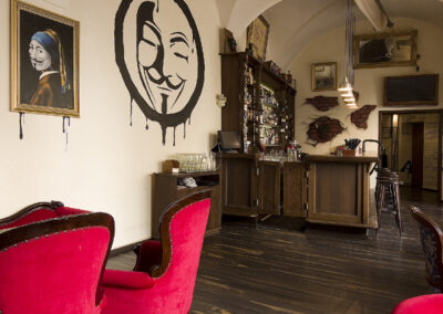 Interiér baru AnonymouS, čalouněné sezení, červená lenoška, tmavé dřevo, obraz na zdi, logo na zdi, bar