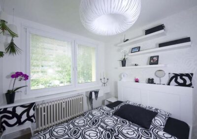 Interiér panelákového bytu, ložnice, bílé police na zdi, okno, závěsné světlo