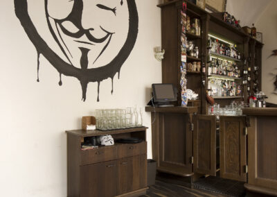 Interiér baru AnonymouS, čalouněné sezení, tmavé dřevo, obraz na zdi, logo na zdi, bar