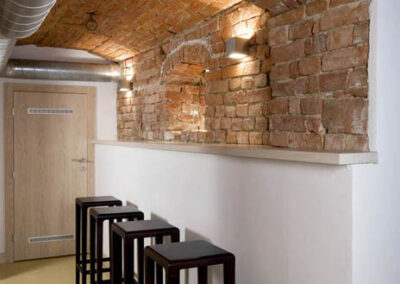 Interiér baru v Poděbradech, cihlové klenby, cihlové zdi, světlá litá podlaha, tmavé dřevo, barové židle, pult, chodba, vzduchotechnika