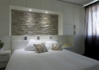 Interiér bytu Řešovská, panelákový byt, kompletní rekonstrukce, ložnice, světlá ložnice, skříně okolo postele, noční stolky, kamenný obklad za postelí, béžový kámen na zdi, osvětlení postele
