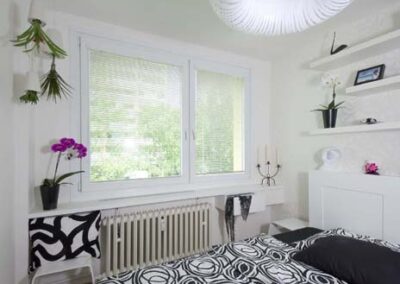 Interiér panelákového bytu, ložnice, bílé police na zdi, okno, závěsné světlo