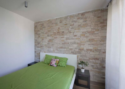 Interiér cihlového bytu, ložnice, kamenný obklad, postel, noční stolky