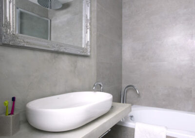 Interiér bytu Řešovská, panelákový byt, kompletní rekonstrukce, koupelna, šedý obklad, šedá cementová stěrka, umyvadlo na desce, vana, zrcadlo ve stříbrném rámu