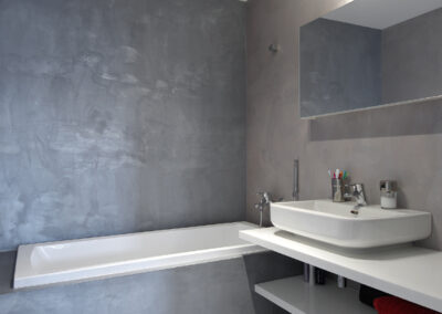 Byt v novostavbě, koupelna, betonová stěrka, vana, umyvadlo, nástěnné zrcadlo, police pod umyvadlem