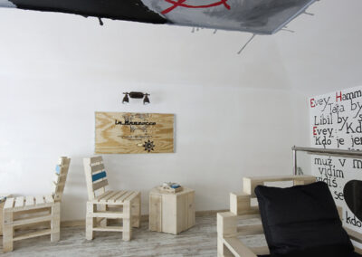 Interiér kavárny AnonymouS, grafika na zdi, dřevěný nábytek, modré pruhy, malba na stropě, sezení na dřevěném nábytku