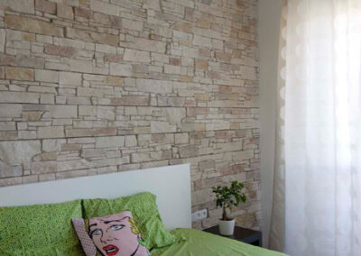 Interiér cihlového bytu, ložnice, kamenný obklad, postel, noční stolky