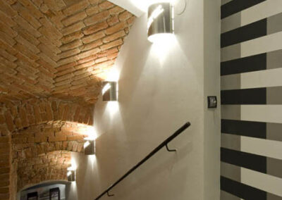 Interiér baru v Poděbradech, bílá zeď, nástěnné osvětlení, černé schodiště, zábradlí, osvětlení schodiště, osvětlení cihlové klenby