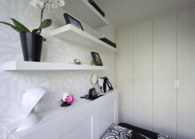 Interiér panelákového bytu, ložnice, bílé police na zdi, závěsné světlo, krémová šatní skříň, tapeta s odlesky