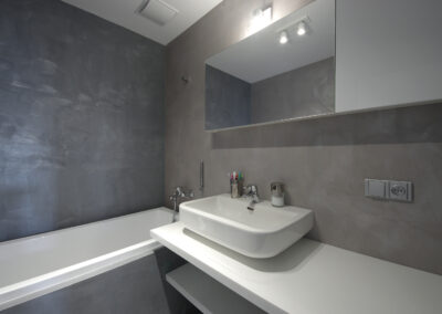 Byt v novostavbě, koupelna, betonová stěrka, vana, umyvadlo, nástěnné zrcadlo, police pod umyvadlem